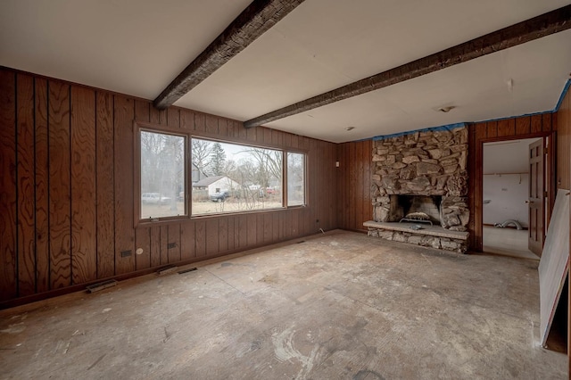 unfurnished living room with beam ceiling, a stone fireplace, and wooden walls