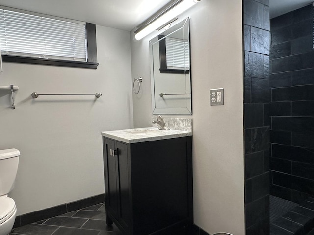 bathroom featuring tile patterned flooring, vanity, a tile shower, and toilet