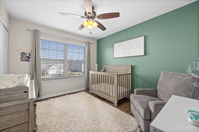 bedroom with a nursery area, ceiling fan, a closet, and hardwood / wood-style flooring