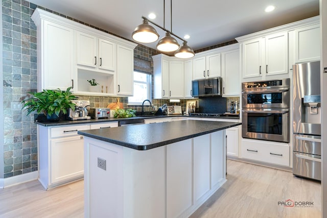 kitchen with white cabinetry, hanging light fixtures, appliances with stainless steel finishes, a kitchen island, and light hardwood / wood-style floors