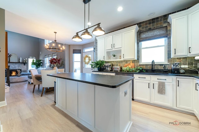 kitchen with white cabinetry, sink, a stone fireplace, and hanging light fixtures