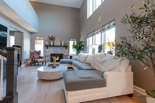 living room with a stone fireplace, a healthy amount of sunlight, light hardwood / wood-style floors, and a towering ceiling