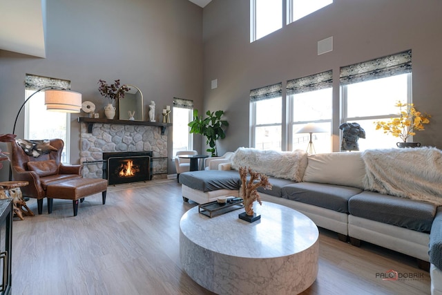 living room featuring a stone fireplace, light hardwood / wood-style flooring, and a towering ceiling