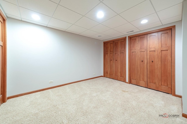 unfurnished bedroom with two closets, light carpet, and a paneled ceiling