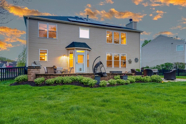 back house at dusk with a yard, an outdoor hangout area, solar panels, and a patio area