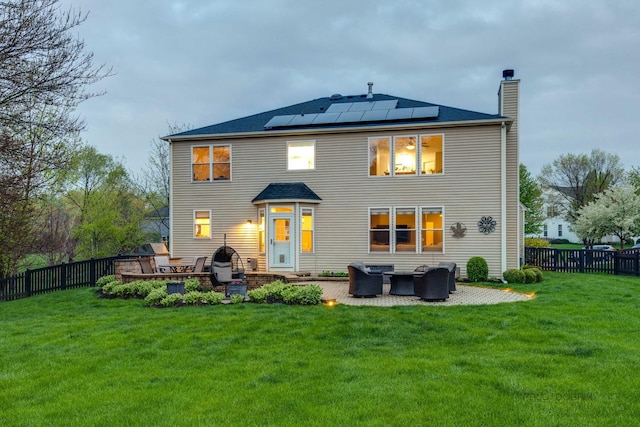 rear view of property featuring a lawn, a patio, and solar panels