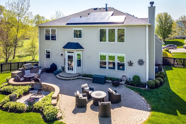 back of house featuring a lawn, an outdoor living space with a fire pit, a patio, and solar panels