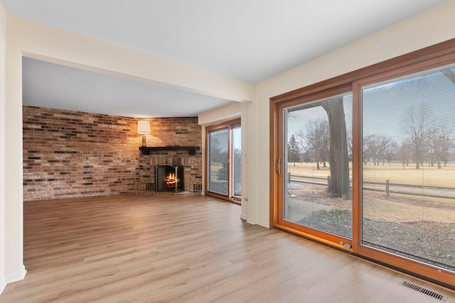 unfurnished living room featuring brick wall, light hardwood / wood-style floors, and a brick fireplace