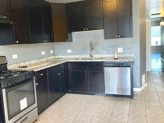 kitchen with stainless steel appliances, sink, light tile patterned floors, and light stone counters