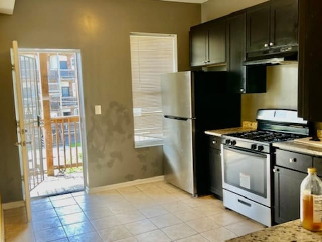 kitchen with light tile patterned flooring, appliances with stainless steel finishes, light stone counters, and dark brown cabinetry