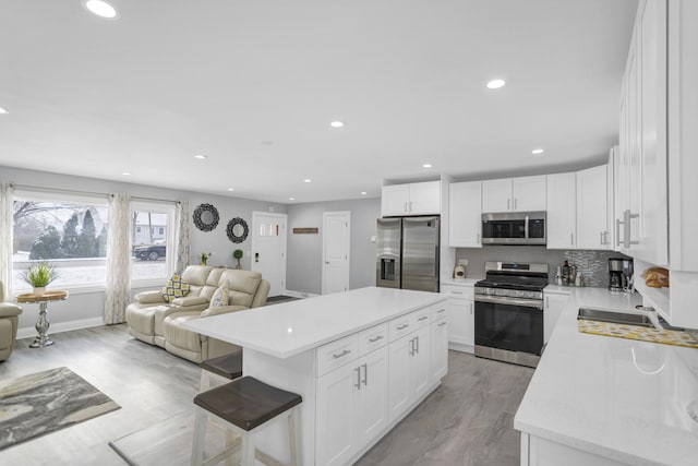 kitchen featuring stainless steel appliances, a kitchen breakfast bar, tasteful backsplash, white cabinets, and a kitchen island