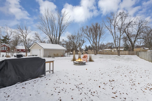 yard layered in snow with a garage, an outdoor structure, and an outdoor fire pit