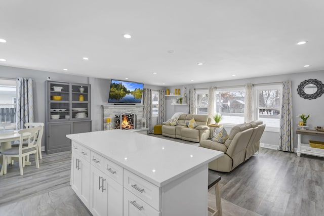 kitchen featuring wood-type flooring, a stone fireplace, a kitchen breakfast bar, and white cabinets