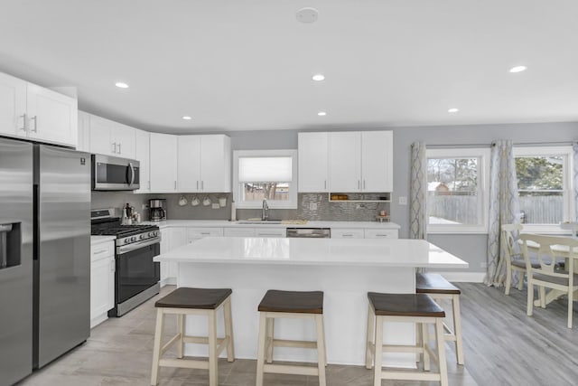 kitchen with sink, a breakfast bar area, appliances with stainless steel finishes, white cabinetry, and a center island