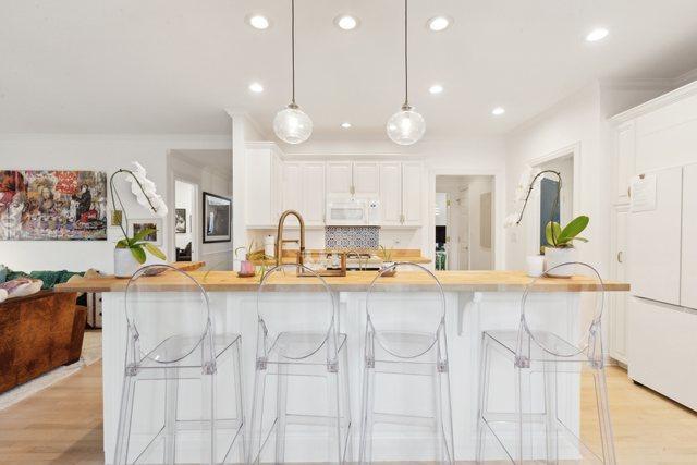 kitchen with a breakfast bar, a fireplace, white cabinetry, wooden counters, and hanging light fixtures