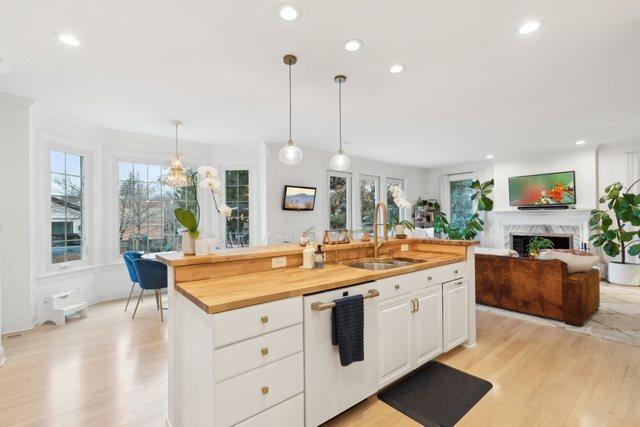 kitchen featuring sink, wooden counters, an island with sink, pendant lighting, and white cabinets