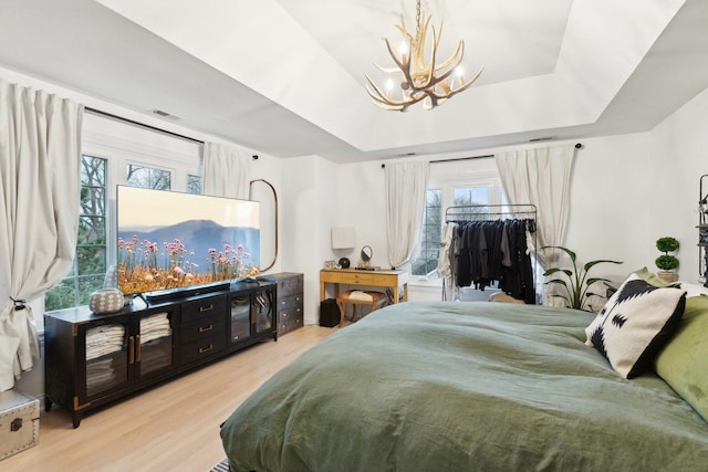 bedroom featuring multiple windows, light wood-type flooring, and a tray ceiling