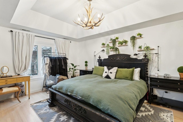 bedroom featuring an inviting chandelier, a raised ceiling, and light hardwood / wood-style flooring