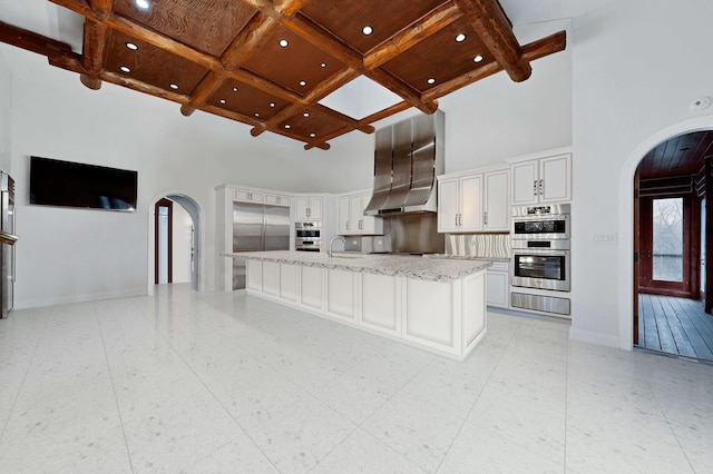 kitchen featuring a towering ceiling, white cabinets, coffered ceiling, stainless steel appliances, and a spacious island