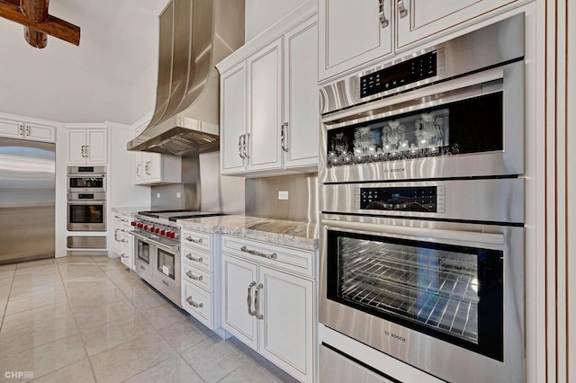 kitchen with appliances with stainless steel finishes, white cabinetry, light stone counters, extractor fan, and light tile patterned flooring