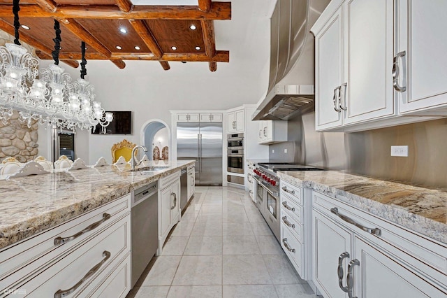 kitchen featuring white cabinetry, hanging light fixtures, high end appliances, wall chimney range hood, and beam ceiling