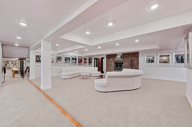 carpeted living room featuring a stone fireplace and a raised ceiling