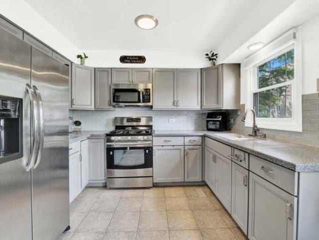 kitchen with light tile patterned flooring, sink, gray cabinetry, decorative backsplash, and stainless steel appliances