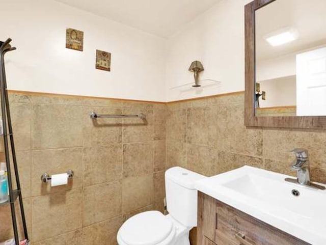 bathroom featuring vanity, toilet, and tile walls