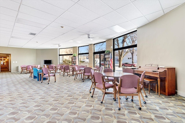 carpeted dining area with a paneled ceiling, plenty of natural light, and floor to ceiling windows