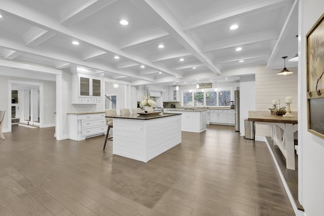 kitchen with dark wood-type flooring, a center island, a kitchen breakfast bar, beamed ceiling, and white cabinets