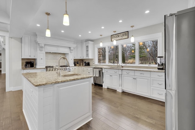 kitchen with appliances with stainless steel finishes, a kitchen island with sink, hanging light fixtures, and white cabinets