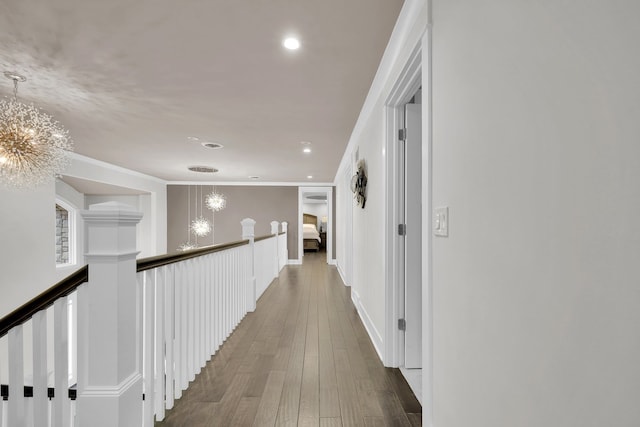 corridor with wood-type flooring, ornamental molding, and a notable chandelier