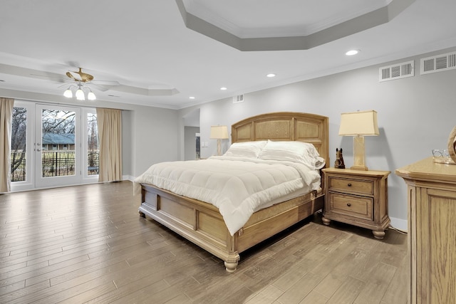 bedroom with ceiling fan, access to exterior, a tray ceiling, wood-type flooring, and ornamental molding