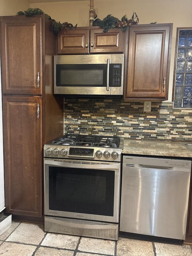 kitchen with appliances with stainless steel finishes, dark brown cabinets, backsplash, and light stone counters