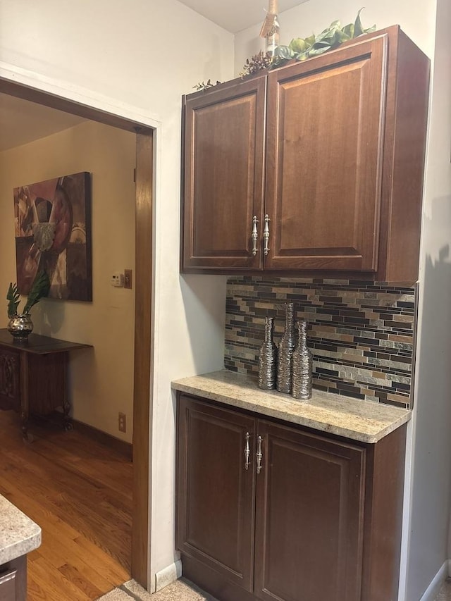 bar with dark brown cabinetry, decorative backsplash, and light hardwood / wood-style flooring