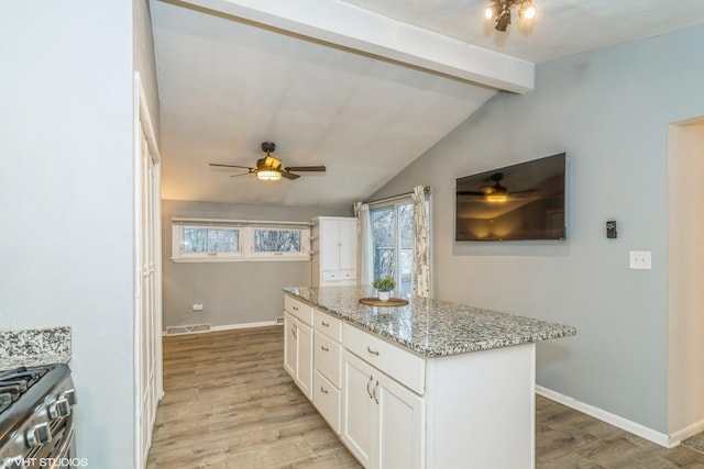 kitchen with light hardwood / wood-style flooring, white cabinetry, stainless steel gas stove, light stone counters, and lofted ceiling with beams