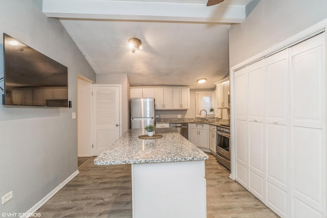 kitchen featuring appliances with stainless steel finishes, white cabinetry, a center island, light stone counters, and light hardwood / wood-style flooring