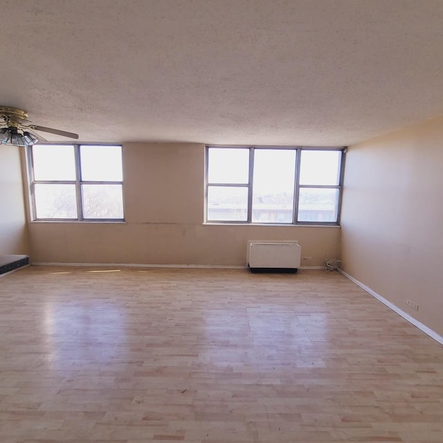 empty room with ceiling fan, light wood-type flooring, and a textured ceiling