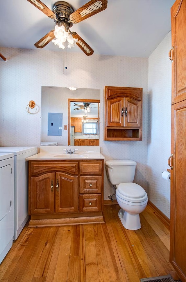 bathroom featuring hardwood / wood-style floors, vanity, electric panel, independent washer and dryer, and toilet