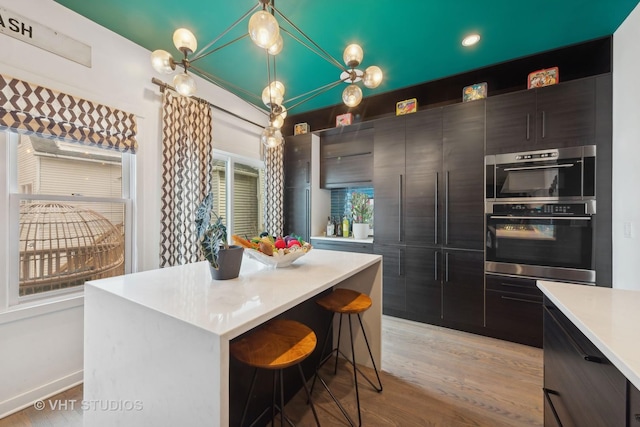 kitchen with pendant lighting, a breakfast bar area, a center island, light hardwood / wood-style floors, and stainless steel double oven