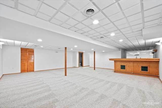 basement featuring light carpet, bar, and a drop ceiling