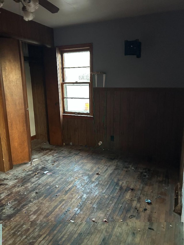 unfurnished bedroom featuring wooden walls, ceiling fan, dark hardwood / wood-style floors, and a closet