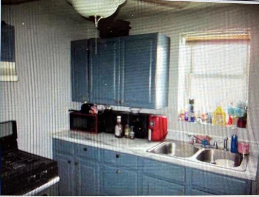 kitchen featuring blue cabinetry, black stove, and sink