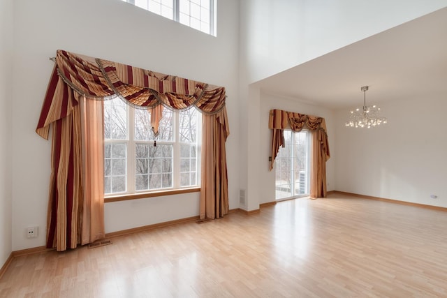 unfurnished room featuring a healthy amount of sunlight, a towering ceiling, a chandelier, and light wood-type flooring