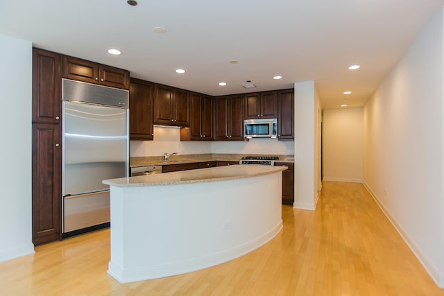 kitchen featuring dark brown cabinetry, a kitchen island, light hardwood / wood-style floors, and appliances with stainless steel finishes