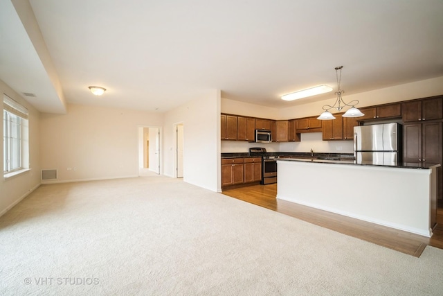 kitchen featuring sink, hanging light fixtures, stainless steel appliances, a center island with sink, and light colored carpet