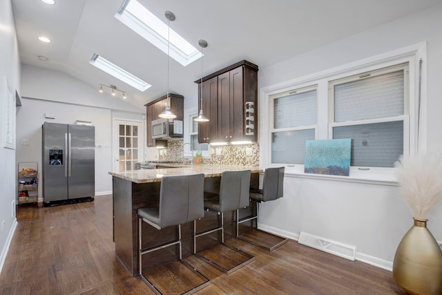 kitchen with vaulted ceiling with skylight, backsplash, hanging light fixtures, kitchen peninsula, and stainless steel appliances