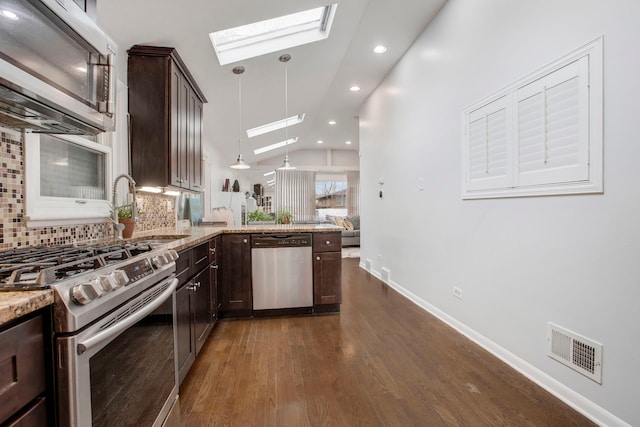 kitchen featuring dark brown cabinets, hanging light fixtures, stainless steel appliances, vaulted ceiling with skylight, and light stone countertops