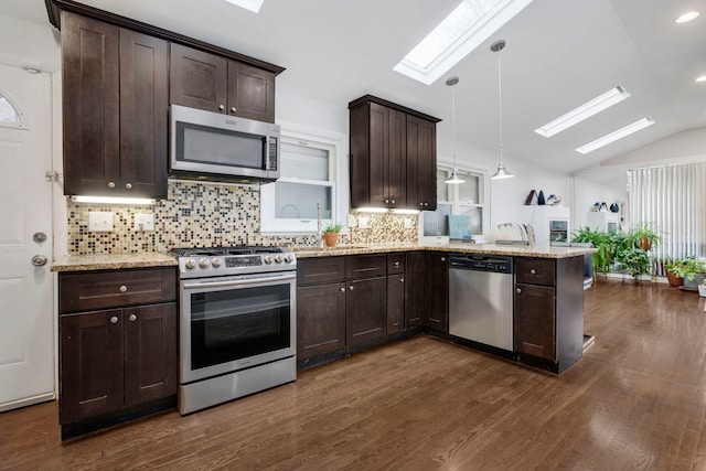 kitchen featuring dark wood-type flooring, lofted ceiling with skylight, decorative light fixtures, appliances with stainless steel finishes, and backsplash