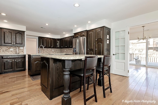 kitchen featuring dark brown cabinets, a center island, stainless steel fridge, and light wood-type flooring